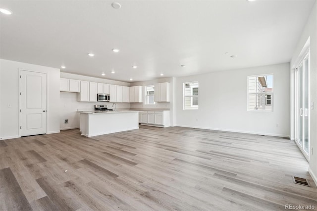 unfurnished living room featuring light wood-type flooring, visible vents, a sink, recessed lighting, and baseboards