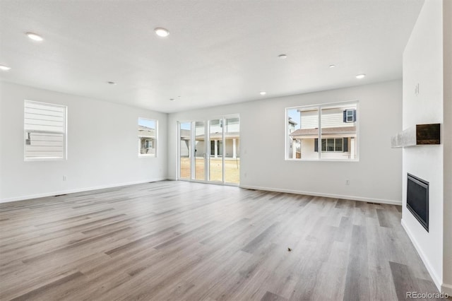 unfurnished living room with recessed lighting, baseboards, a large fireplace, and light wood-style floors