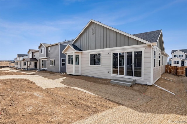 back of property with fence, roof with shingles, entry steps, board and batten siding, and a residential view