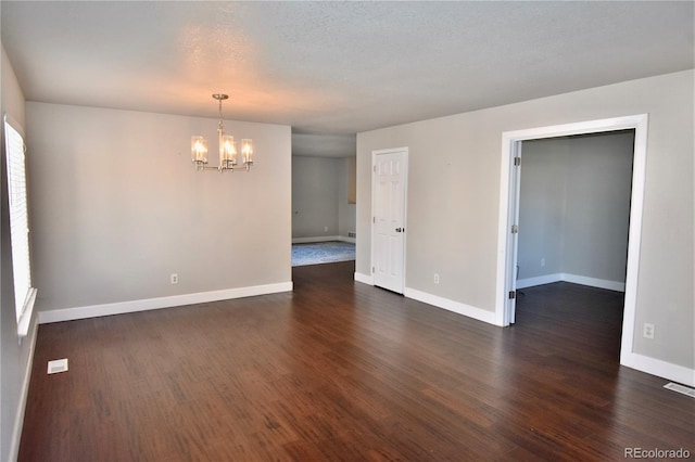 empty room with a notable chandelier, a textured ceiling, and dark wood-type flooring