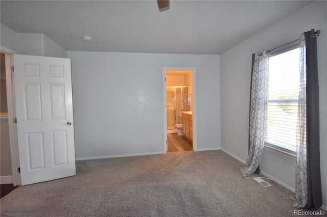 unfurnished bedroom with light carpet, multiple windows, and ensuite bath