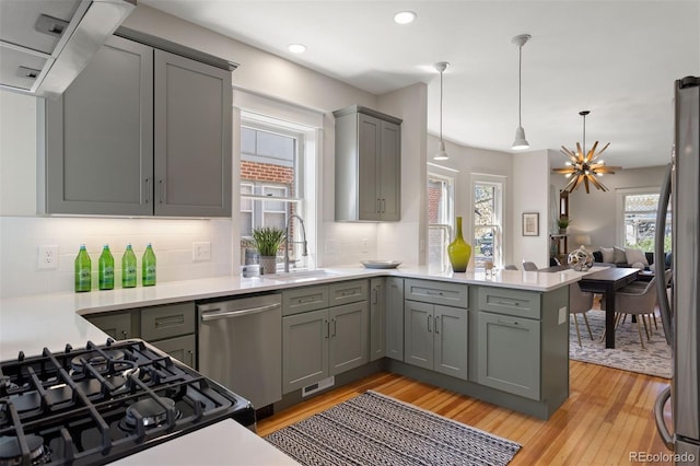 kitchen with kitchen peninsula, light hardwood / wood-style flooring, pendant lighting, gray cabinetry, and appliances with stainless steel finishes