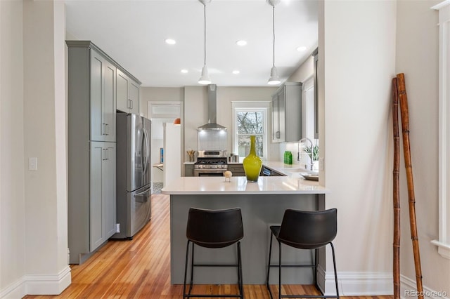 kitchen with sink, wall chimney exhaust hood, gray cabinets, and appliances with stainless steel finishes