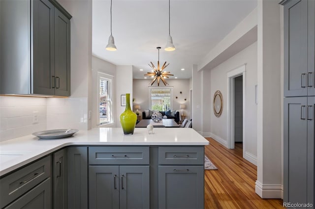 kitchen with decorative light fixtures, gray cabinets, light hardwood / wood-style flooring, and tasteful backsplash