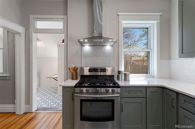 kitchen featuring tasteful backsplash, stainless steel gas stove, wall chimney range hood, and light hardwood / wood-style floors