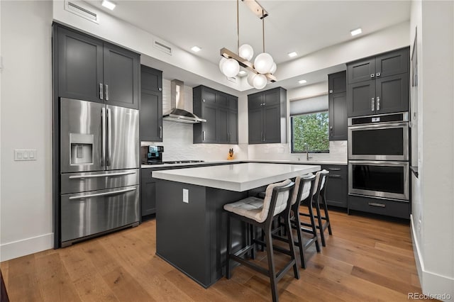 kitchen with a kitchen island, appliances with stainless steel finishes, decorative light fixtures, a kitchen bar, and wall chimney range hood