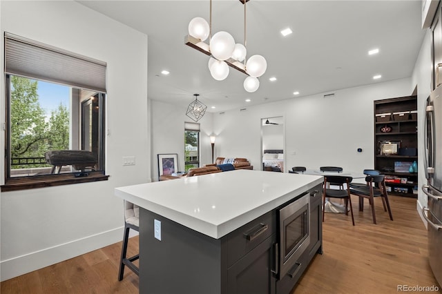 kitchen with light hardwood / wood-style flooring, a kitchen island, a wealth of natural light, pendant lighting, and stainless steel appliances