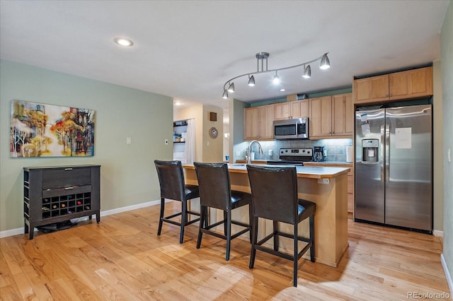 4855 E Atlantic Pl, Denver, CO 80222 - kitchen featuring stainless steel appliances, tasteful backsplash, light countertops, a breakfast bar area, and light wood-style floors