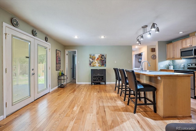 4855 E Atlantic Pl, Denver, CO 80222 - kitchen with appliances with stainless steel finishes, french doors, light wood-style flooring, a kitchen breakfast bar, and tasteful backsplash