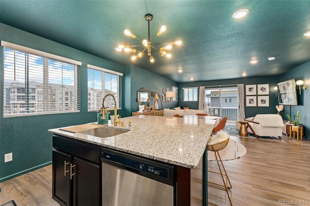 kitchen with an island with sink, light wood-type flooring, sink, light stone counters, and dishwasher