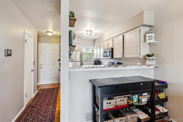 1818 S Quebec Way Unit 4, Denver, CO 80231 - kitchen featuring appliances with stainless steel finishes, wood finished floors, decorative backsplash, light stone countertops, and white cabinets