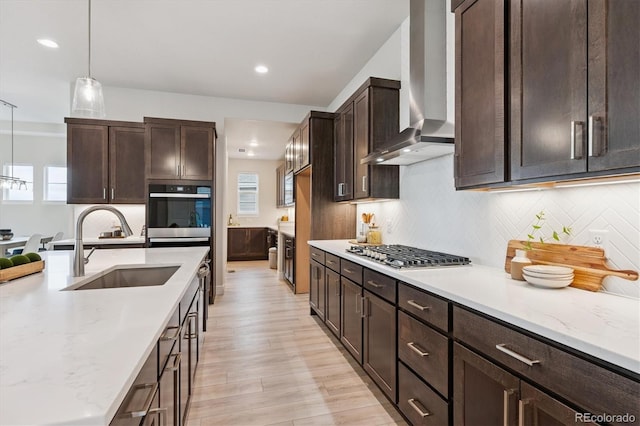22183 E Rocky Top Pl, Aurora, CO 80016 - kitchen featuring wall chimney range hood, stainless steel gas cooktop, dark brown cabinetry, light wood finished floors, and recessed lighting