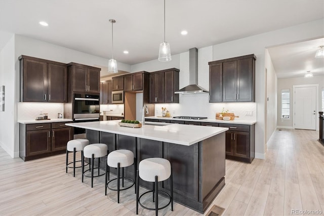 22183 E Rocky Top Pl, Aurora, CO 80016 - kitchen with wall chimney range hood, stainless steel appliances, light wood finished floors, dark brown cabinetry, and recessed lighting