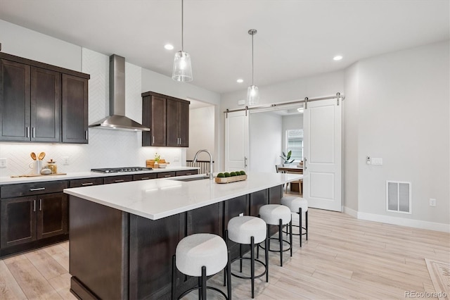 22183 E Rocky Top Pl, Aurora, CO 80016 - kitchen with wall chimney exhaust hood, a barn door, light wood finished floors, stainless steel gas cooktop, and recessed lighting