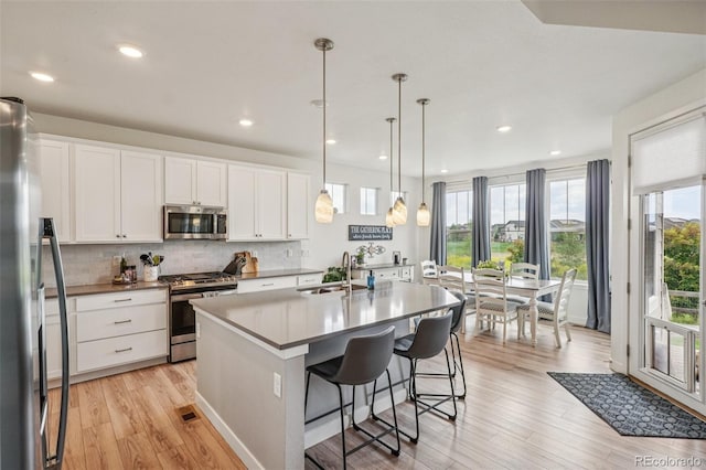 12841 Lake Port St, Longmont, CO 80504 - kitchen featuring stainless steel appliances, light wood-style floors, white cabinets, tasteful backsplash, and a kitchen island with sink