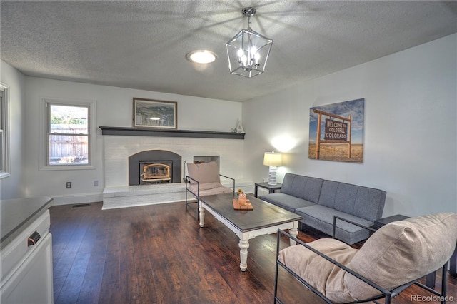living room with wood-type flooring, a notable chandelier, a glass covered fireplace, and a textured ceiling