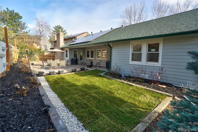 rear view of house with a fenced backyard, a lawn, roof with shingles, a patio area, and solar panels