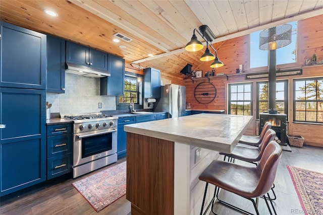 kitchen with visible vents, a wood stove, appliances with stainless steel finishes, under cabinet range hood, and blue cabinets