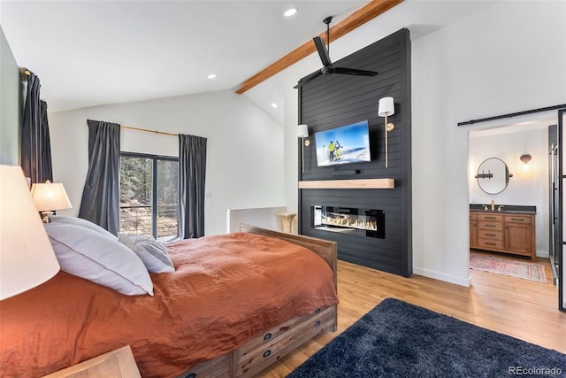 bedroom featuring baseboards, a large fireplace, ensuite bath, light wood-style flooring, and beamed ceiling