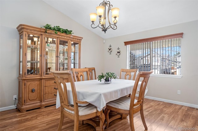 dining area with a notable chandelier, hardwood / wood-style flooring, and vaulted ceiling