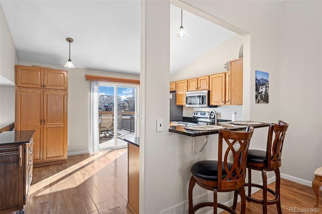 kitchen featuring appliances with stainless steel finishes, a kitchen bar, hanging light fixtures, hardwood / wood-style flooring, and kitchen peninsula