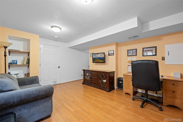 office space with built in features, a textured ceiling, and light wood-type flooring