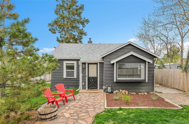 bungalow featuring fence, a shingled roof, and a chimney