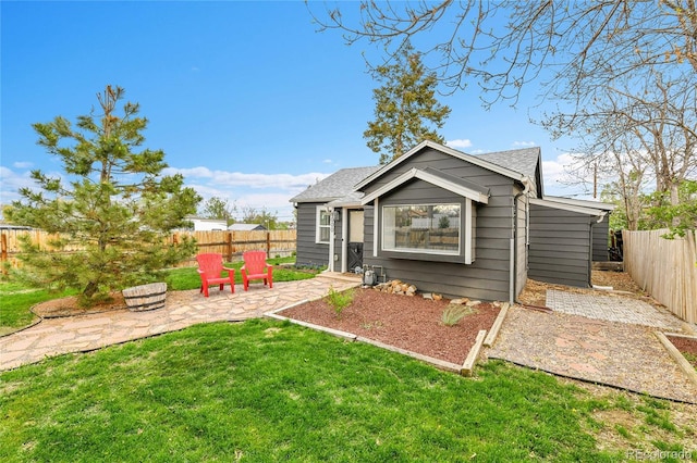 rear view of house with a fenced backyard, a patio area, a yard, and a shingled roof