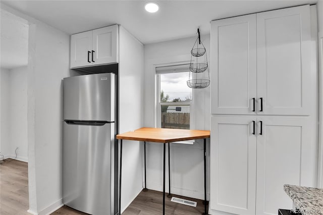 kitchen with freestanding refrigerator, white cabinetry, wood finished floors, and visible vents