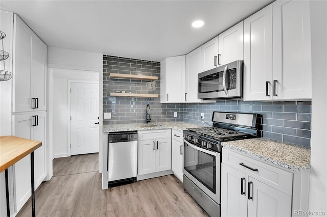 kitchen featuring light wood-type flooring, a sink, open shelves, and appliances with stainless steel finishes