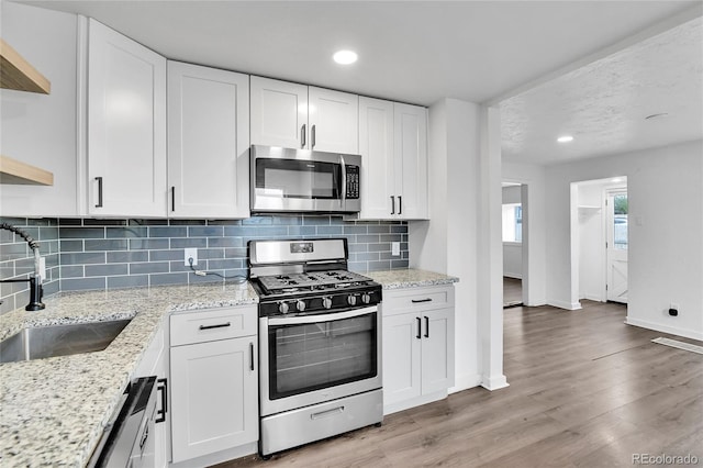 kitchen featuring open shelves, a sink, baseboards, stainless steel appliances, and white cabinetry