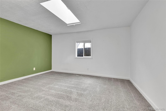 carpeted empty room featuring a textured ceiling, a skylight, and baseboards