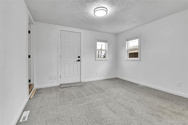 carpeted empty room with visible vents, a textured ceiling, and baseboards