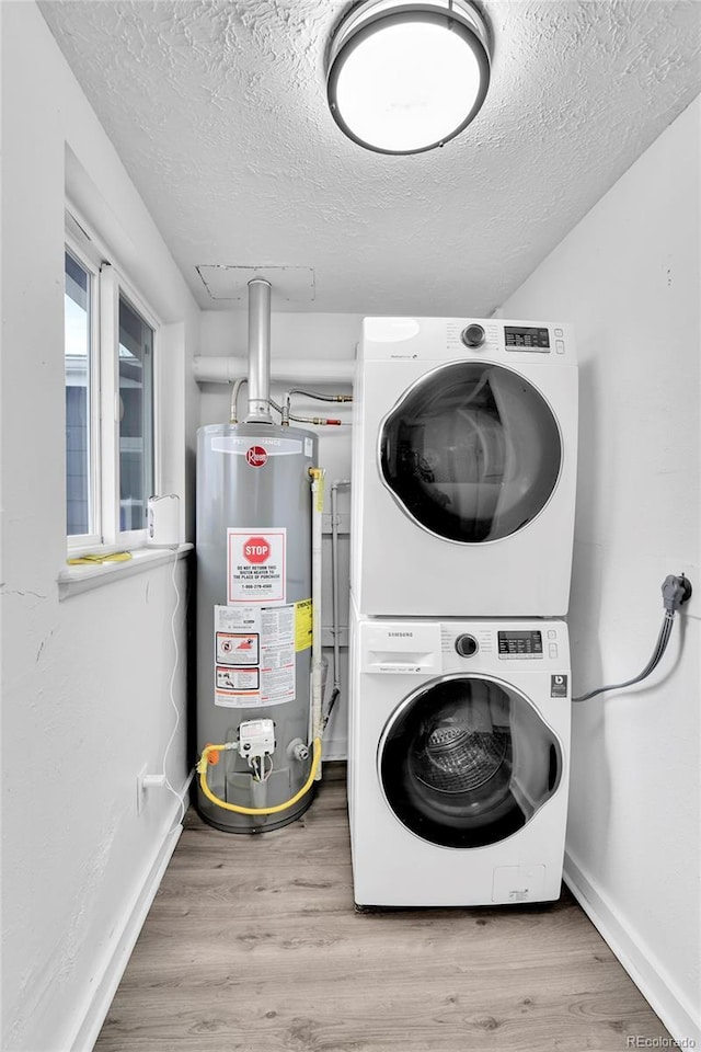 clothes washing area featuring laundry area, a textured ceiling, stacked washing maching and dryer, water heater, and wood finished floors
