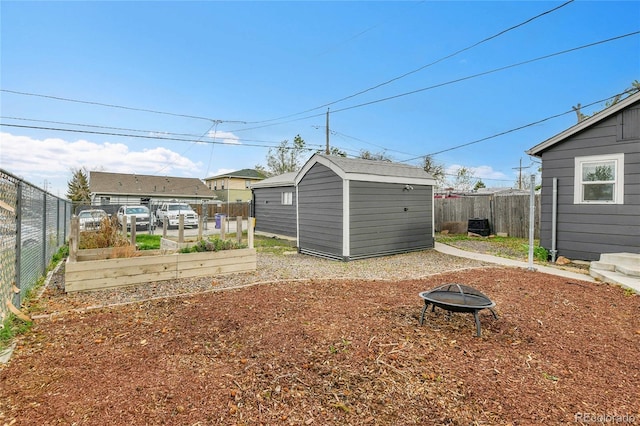 view of yard featuring a storage shed, a garden, a fenced backyard, and a fire pit