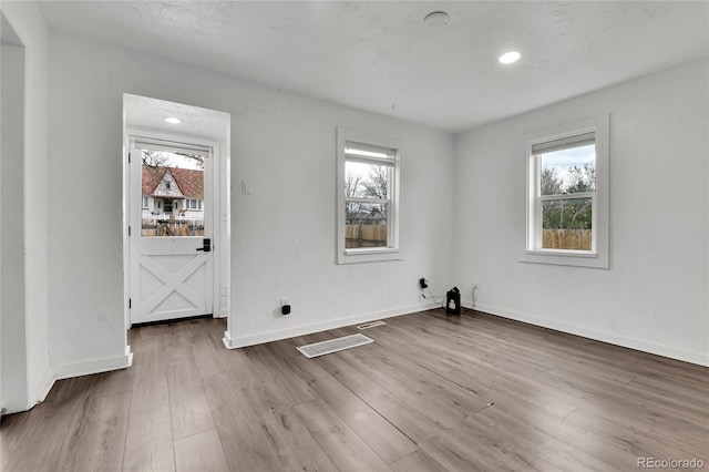 unfurnished room featuring baseboards, recessed lighting, wood finished floors, and a wealth of natural light