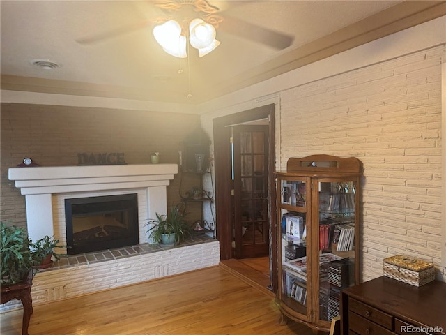 living room featuring ceiling fan, brick wall, wood-type flooring, and a fireplace