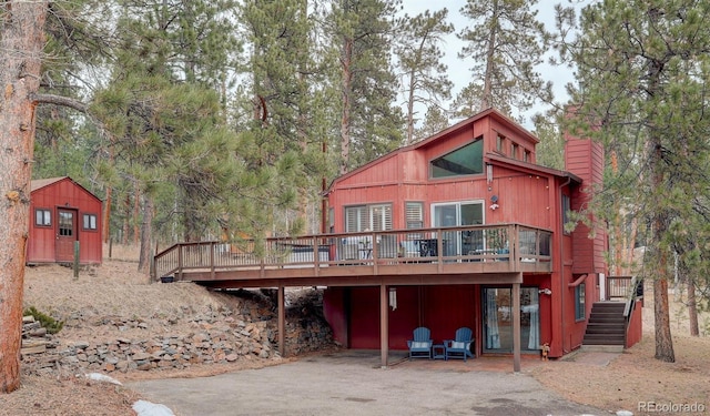 rear view of house featuring an outbuilding, a deck, a storage unit, a chimney, and a patio area