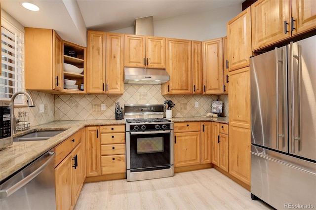 kitchen with light stone counters, under cabinet range hood, stainless steel appliances, a sink, and light wood-style floors