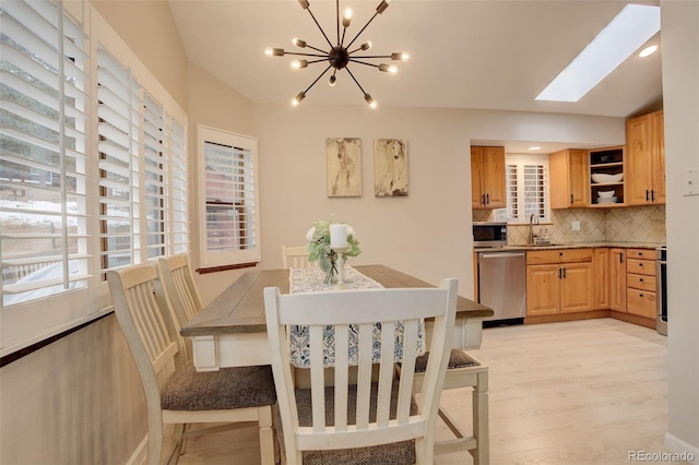 dining room featuring vaulted ceiling with skylight, light wood-style flooring, and a notable chandelier