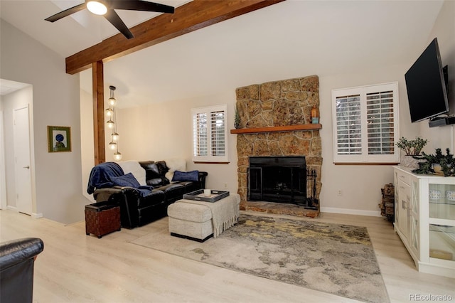 living room with vaulted ceiling with beams, light wood finished floors, a ceiling fan, a stone fireplace, and baseboards