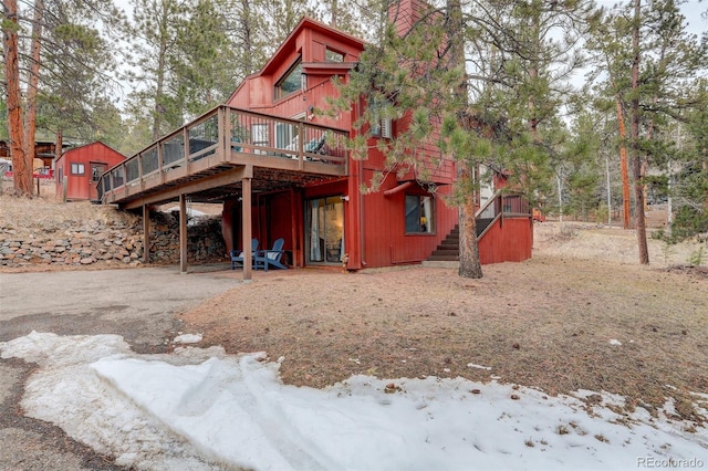 snow covered rear of property with aphalt driveway, a carport, and a wooden deck