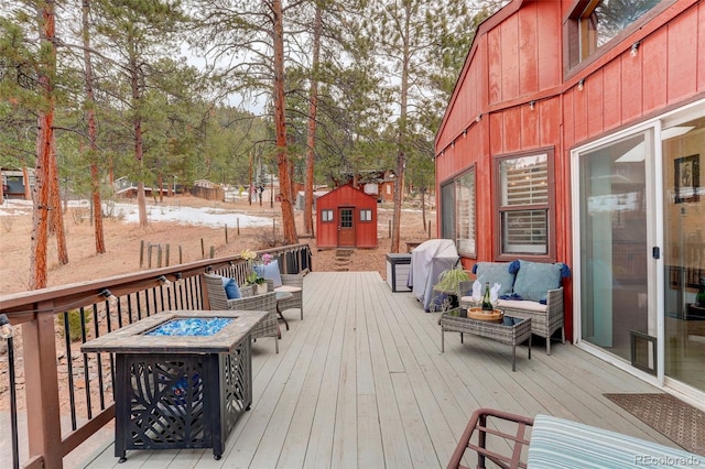 wooden deck with an outdoor living space with a fire pit, a grill, a storage unit, and an outbuilding