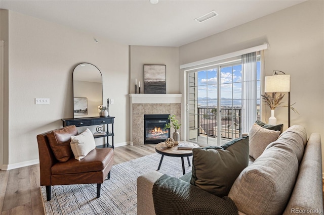 living area featuring baseboards, visible vents, a tiled fireplace, and wood finished floors