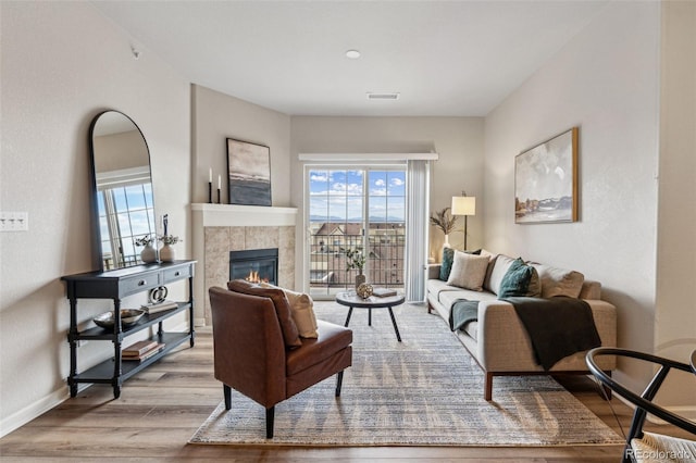 living area featuring baseboards, a tiled fireplace, wood finished floors, and a healthy amount of sunlight