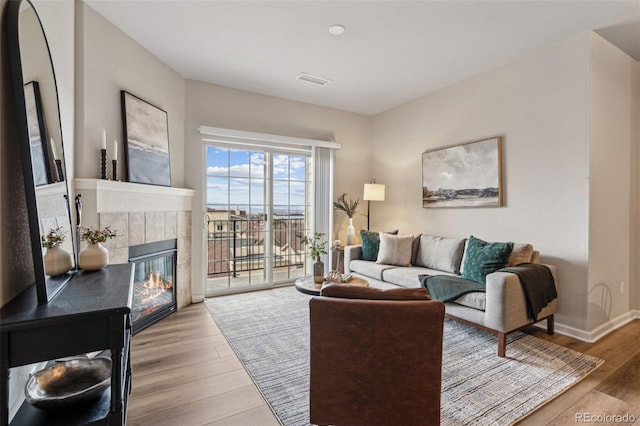 living area with light wood-style floors, baseboards, visible vents, and a tile fireplace