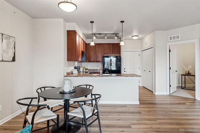 kitchen featuring light wood-style flooring, a peninsula, visible vents, black refrigerator with ice dispenser, and brown cabinetry