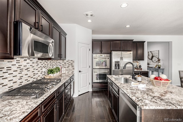 kitchen featuring stainless steel appliances, a sink, light stone countertops, dark brown cabinetry, and dark wood finished floors