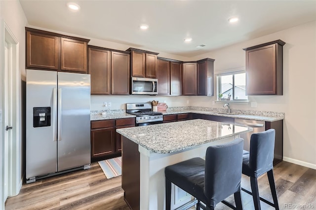 kitchen with a kitchen breakfast bar, a kitchen island, wood finished floors, appliances with stainless steel finishes, and dark brown cabinets