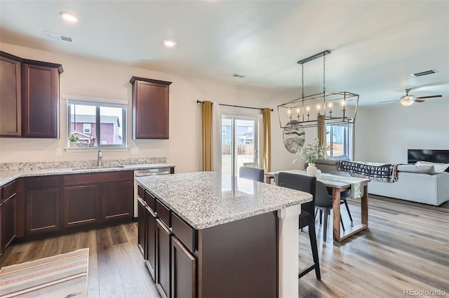 kitchen with a center island, dark brown cabinetry, open floor plan, wood finished floors, and a sink